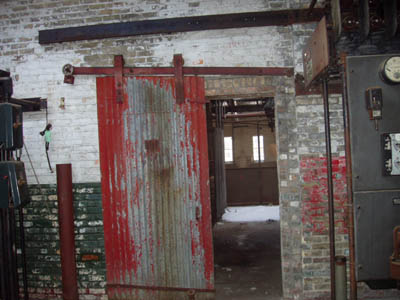 Beyond this door lies a room that seems to have once contained several workshop compartments.